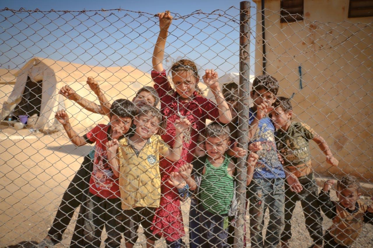 services-02 Children gather behind a fence in a refugee camp in Idlib, Syria, highlighting the challenges faced by refugees.